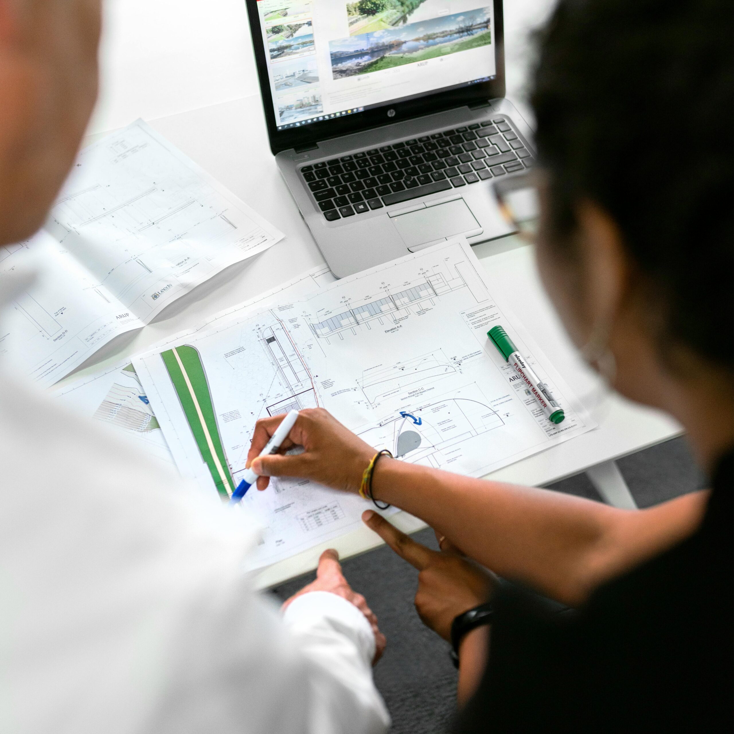 Engineers collaborate on designs with blueprints and laptops in a modern office setting.