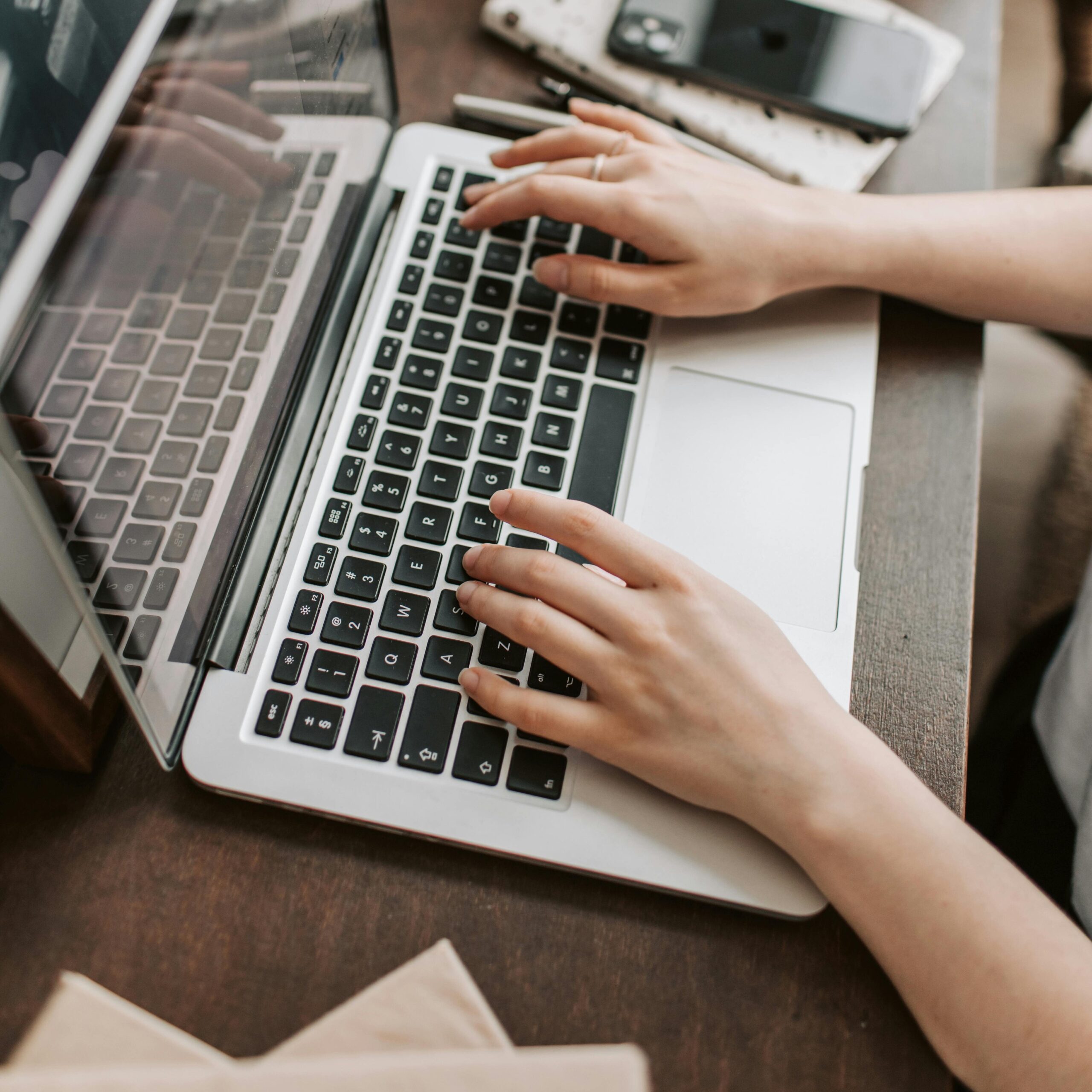 From above of unrecognizable woman sitting at table and typing on keyboard of computer during remote work in modern workspace