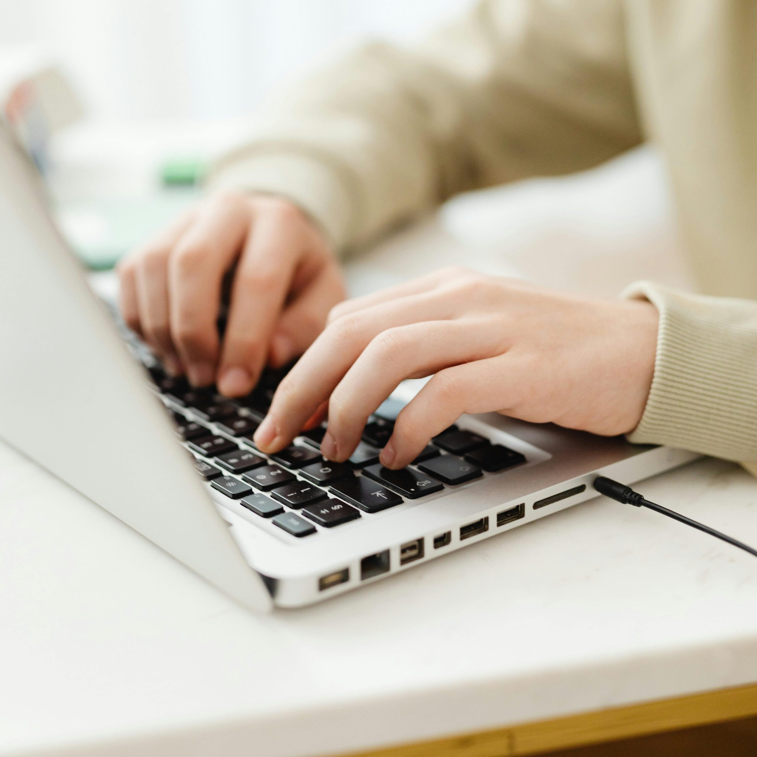 Close-up of hands typing on a laptop, showcasing remote work indoors.